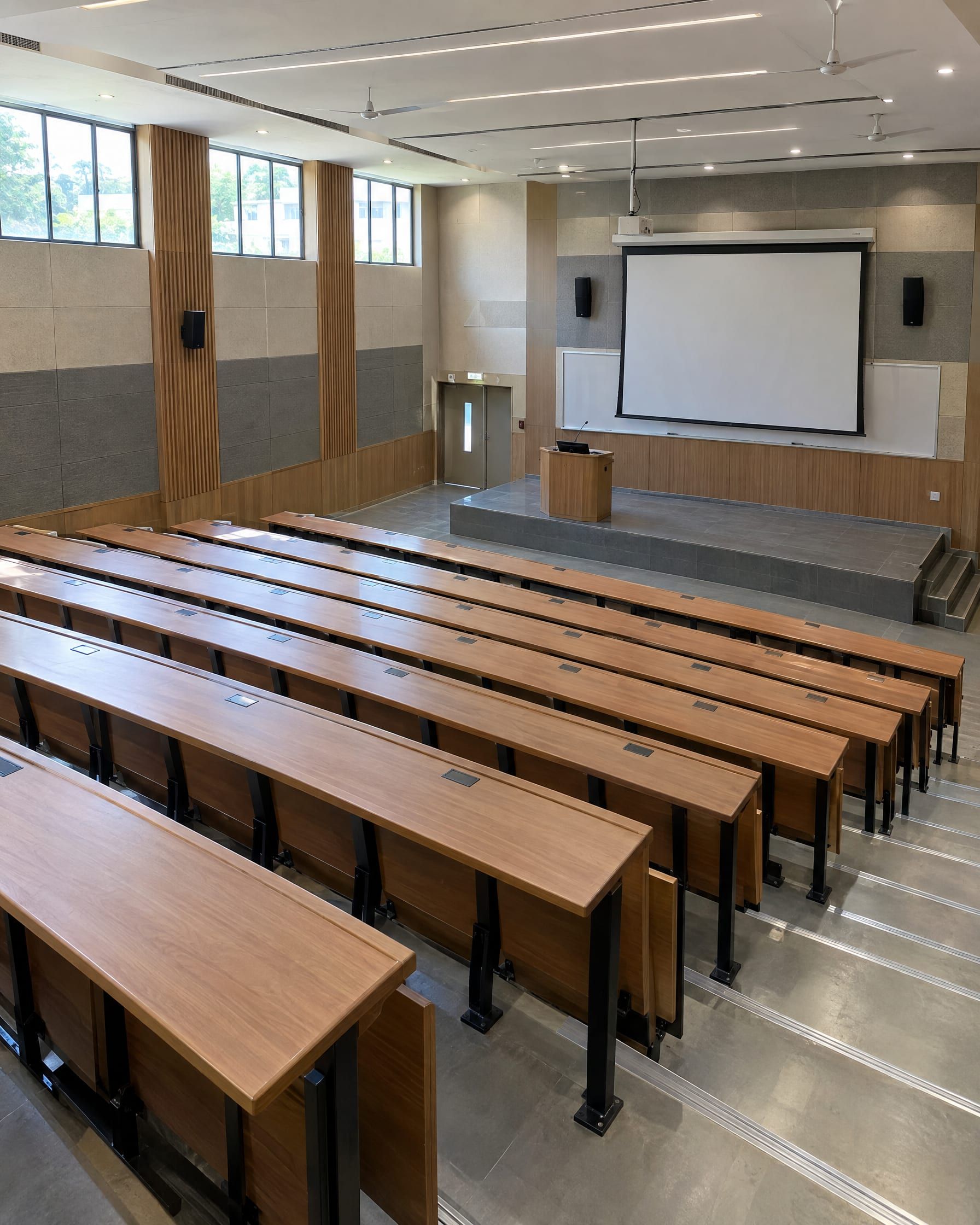 An empty tiered lecture theatre with wooden desks and a projection screen